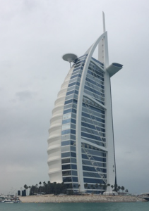 a tall building with a curved roof with Burj Al Arab in the background