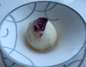 a white ball of ice cream with a rose petal in a bowl