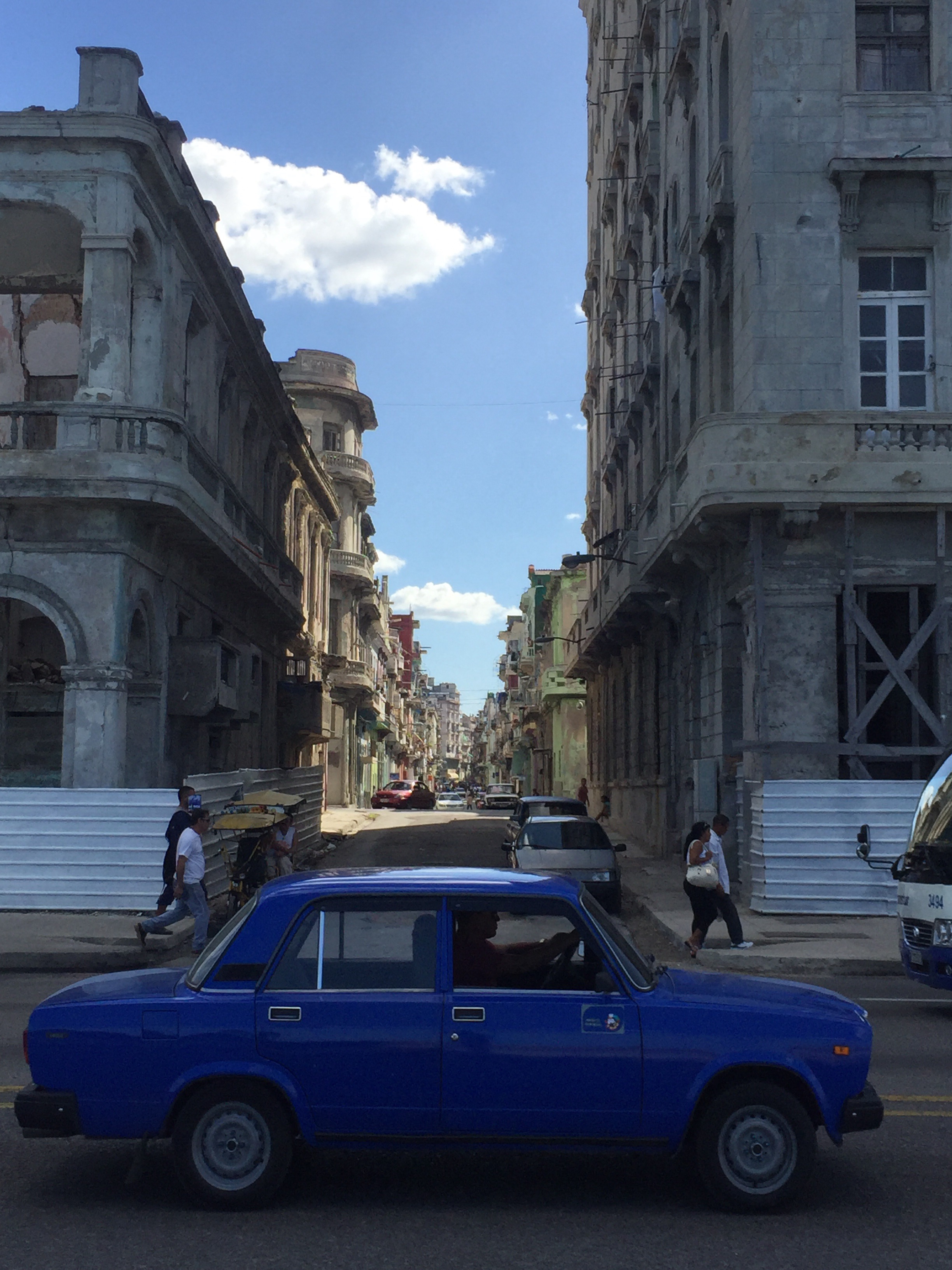 a blue car on a street with buildings and people walking