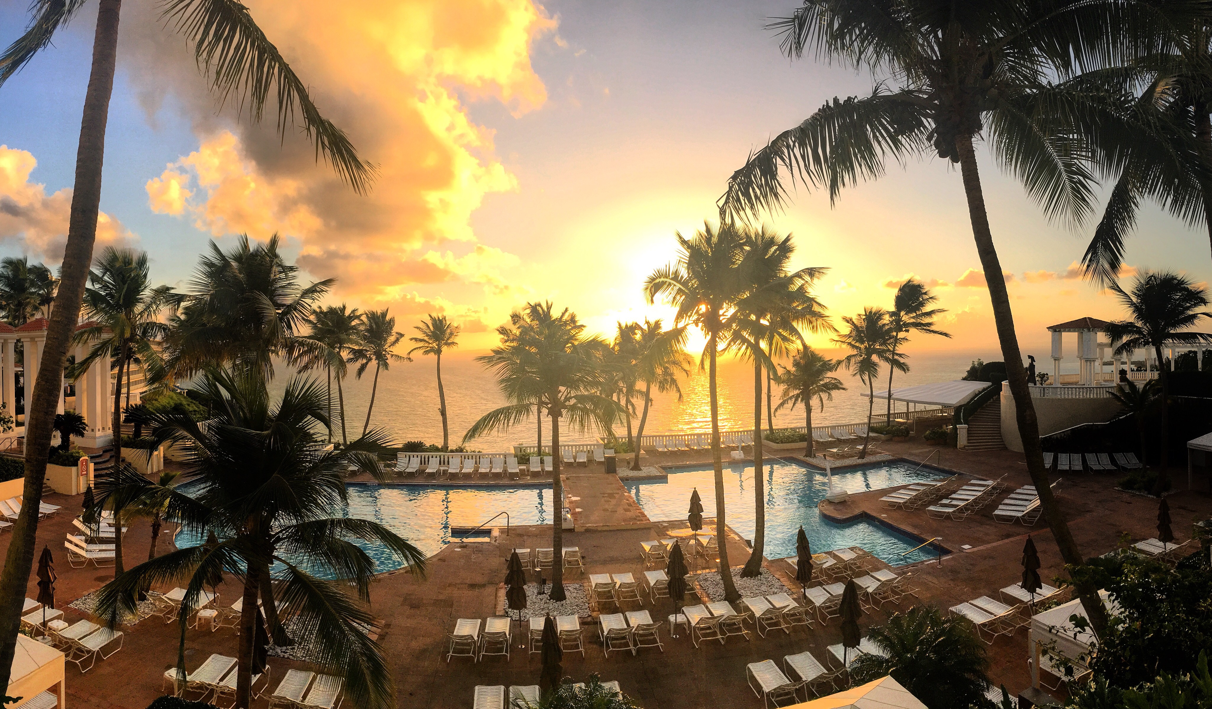 a pool with palm trees and a beach and a sunset