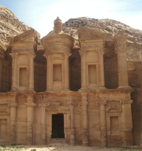 a stone building with columns and a steep hill with Petra in the background