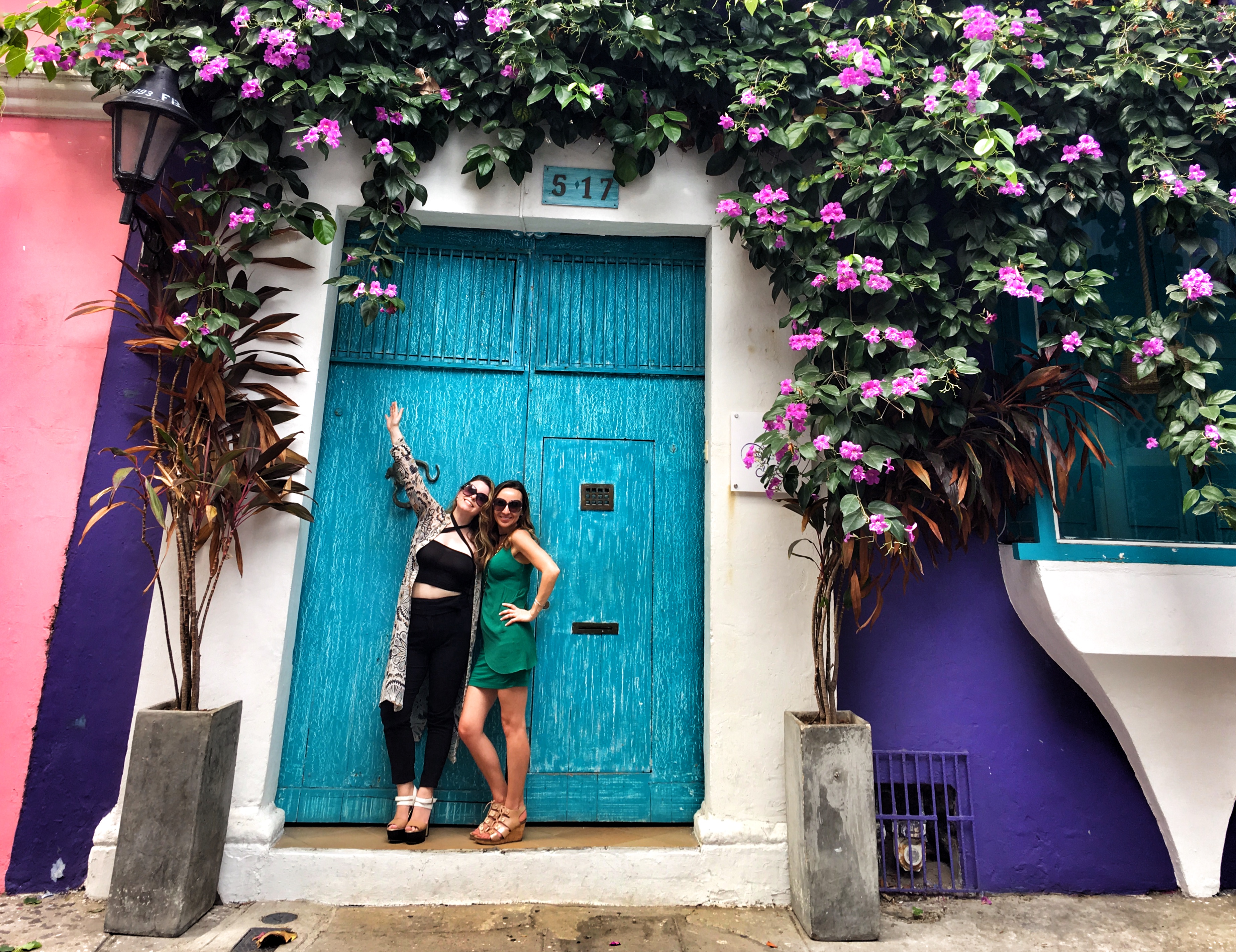 two women standing in front of a blue door with flowers