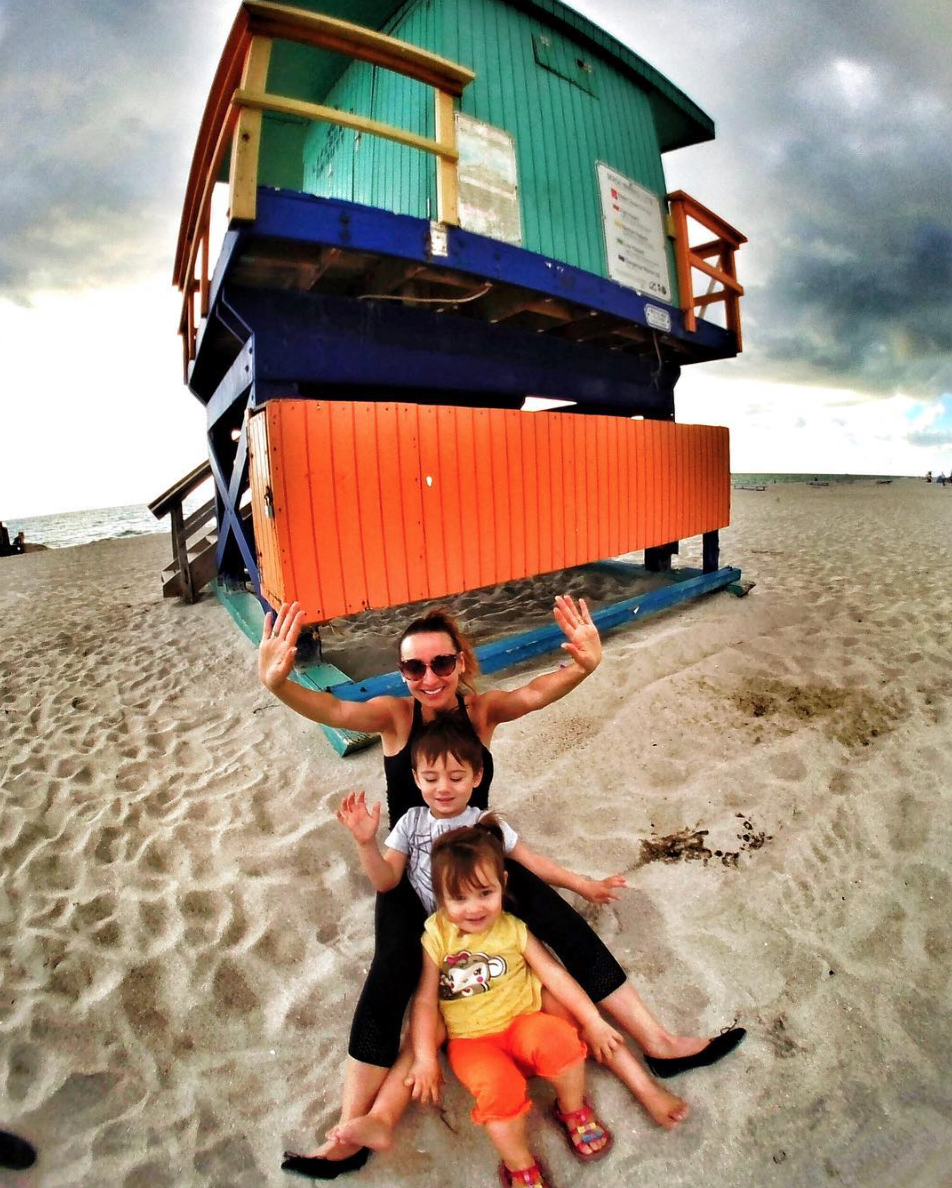 a woman and two children sitting on sand next to a lifeguard hut