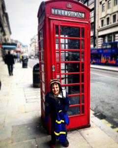 a boy standing in front of a red telephone booth